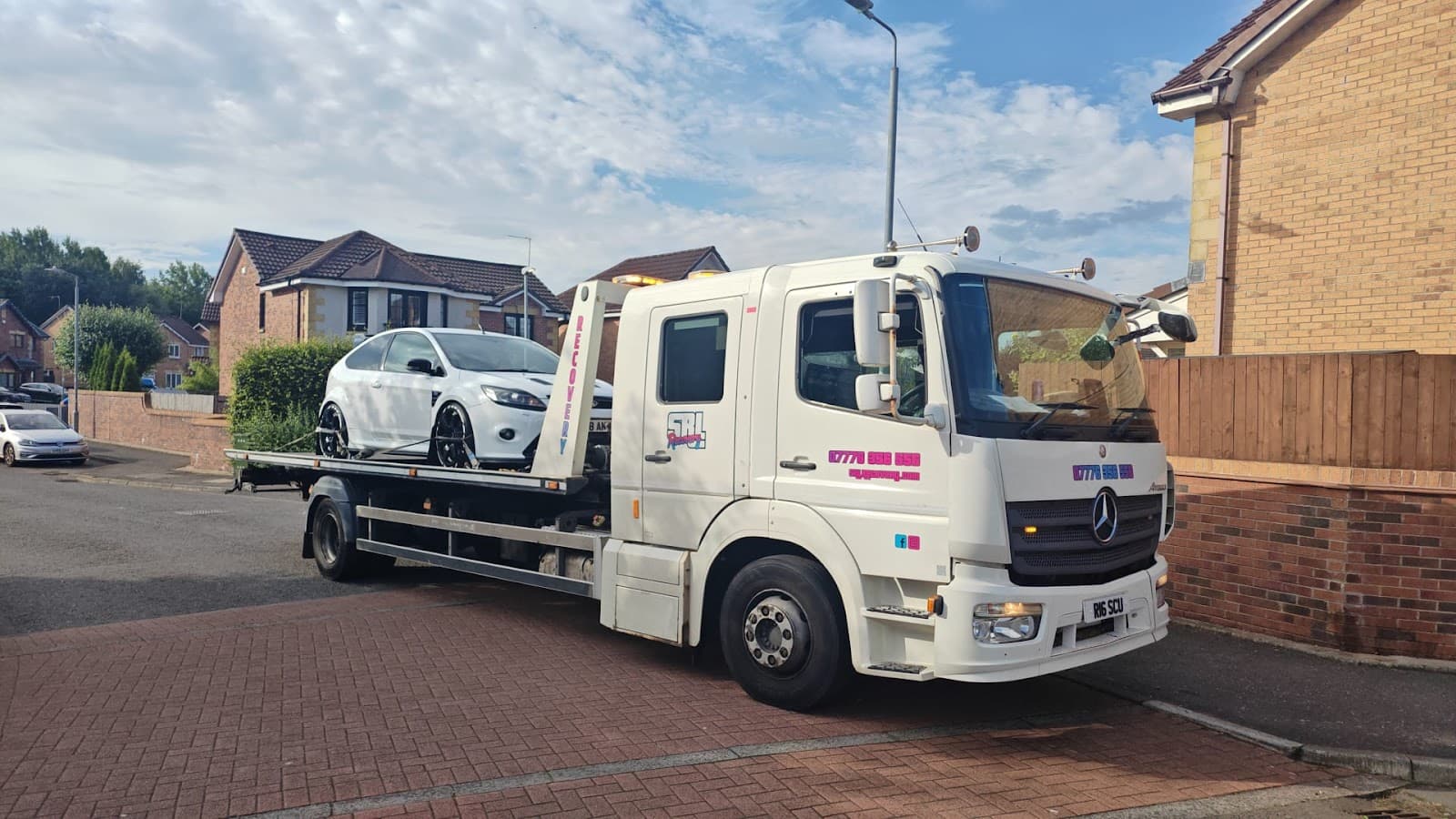 SRL Recovery flatbed truck loading a white Ford Focus on a residential street in Glasgow